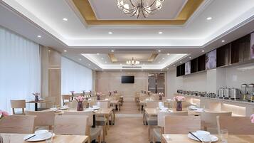 A hotel dining area with multiple tables, chairs, and a chandelier.
