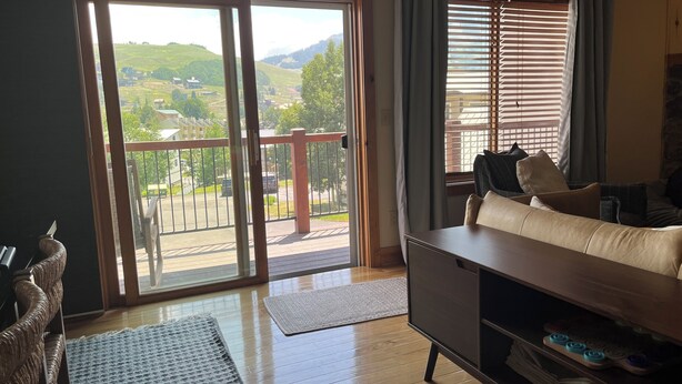 Sala de estar com sofá, mesa de centro, tapete e vista para uma varanda com guarda-corpo.