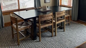 Uma área de refeições com uma mesa de madeira escura, cadeiras de fibra e um candelabro com detalhes de chifres.