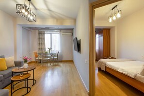 Una habitación de hotel moderna con una cama, un televisor montado en la pared, una zona de comedor con mesa y sillas, y un área de estar con sofá y mesa de centro.