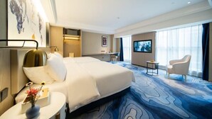 A hotel room with a large bed, a desk, a TV, and a seating area with a chair. - Kyriad Hotel (Zijin Wanhui Branch) (Zijin)