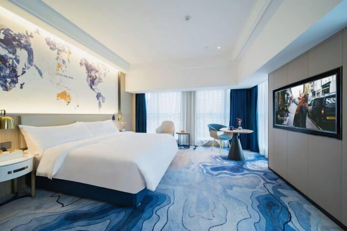 A hotel room with a large bed, a desk, a chair, a small table, and a large world map on the wall.