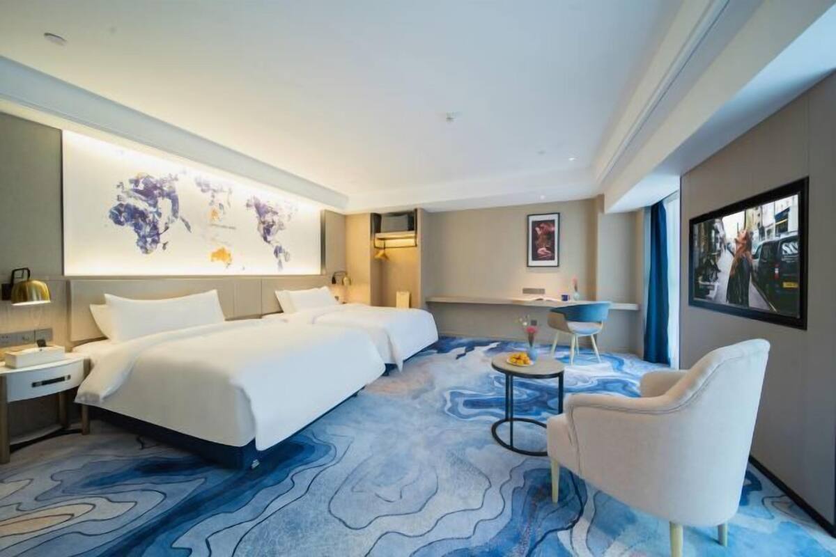 A hotel room with a large bed, a desk, a chair, and a wall-mounted TV.