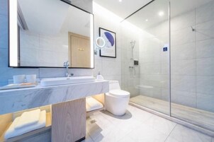 A modern bathroom with a marble sink, a toilet, and a glass-enclosed shower.