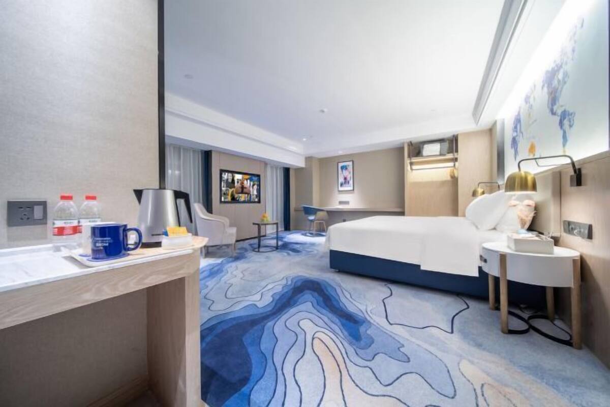 A hotel room with a bed, a desk, a chair, a coffee maker, and a TV.