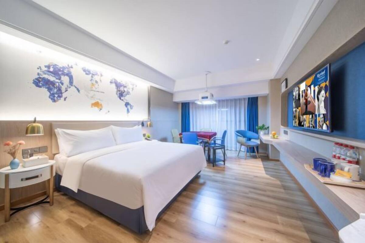 A hotel room with a bed, a desk, a chair, a TV, and a world map on the wall.