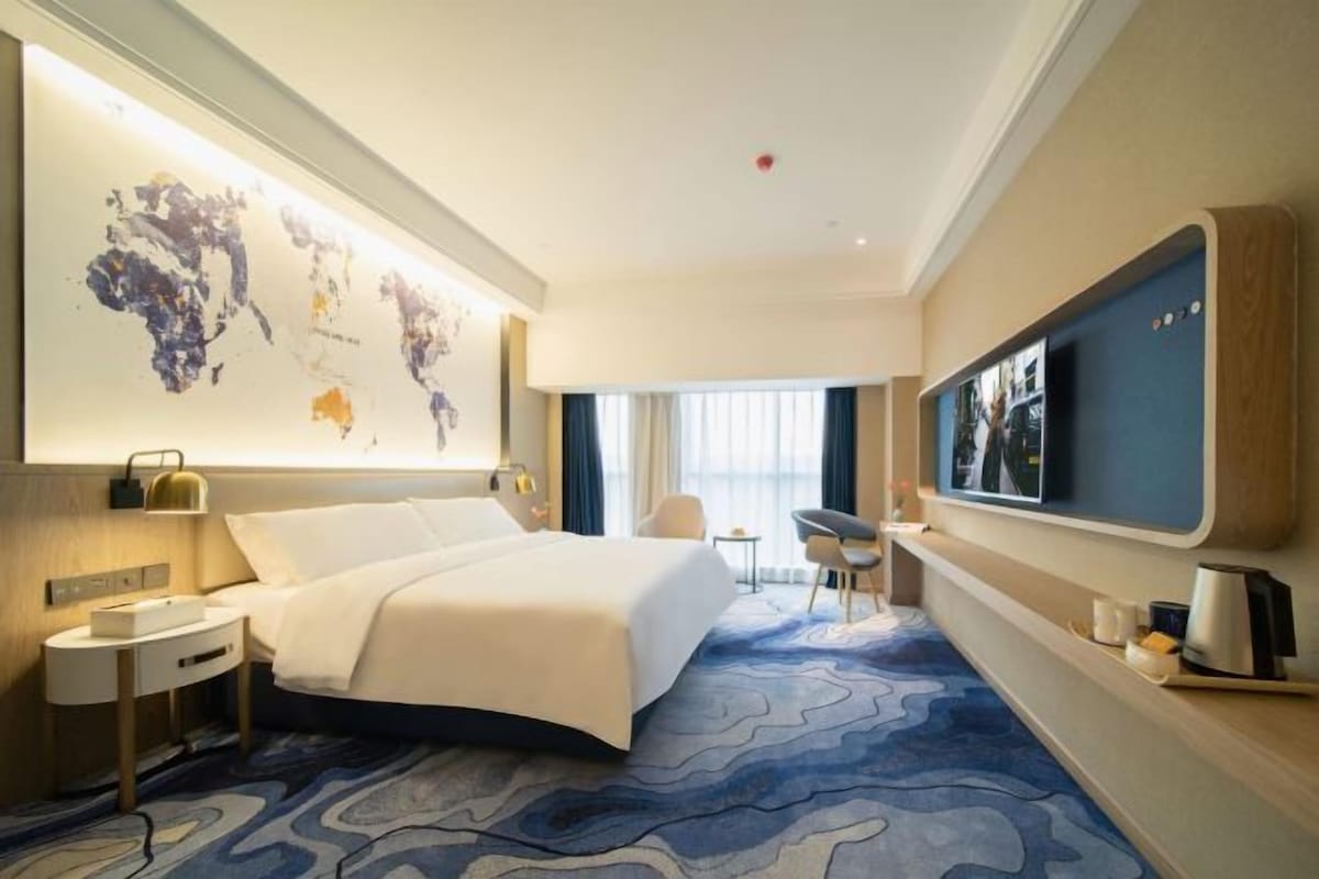 A hotel room with a bed, a desk, a chair, a TV, and a world map on the wall.