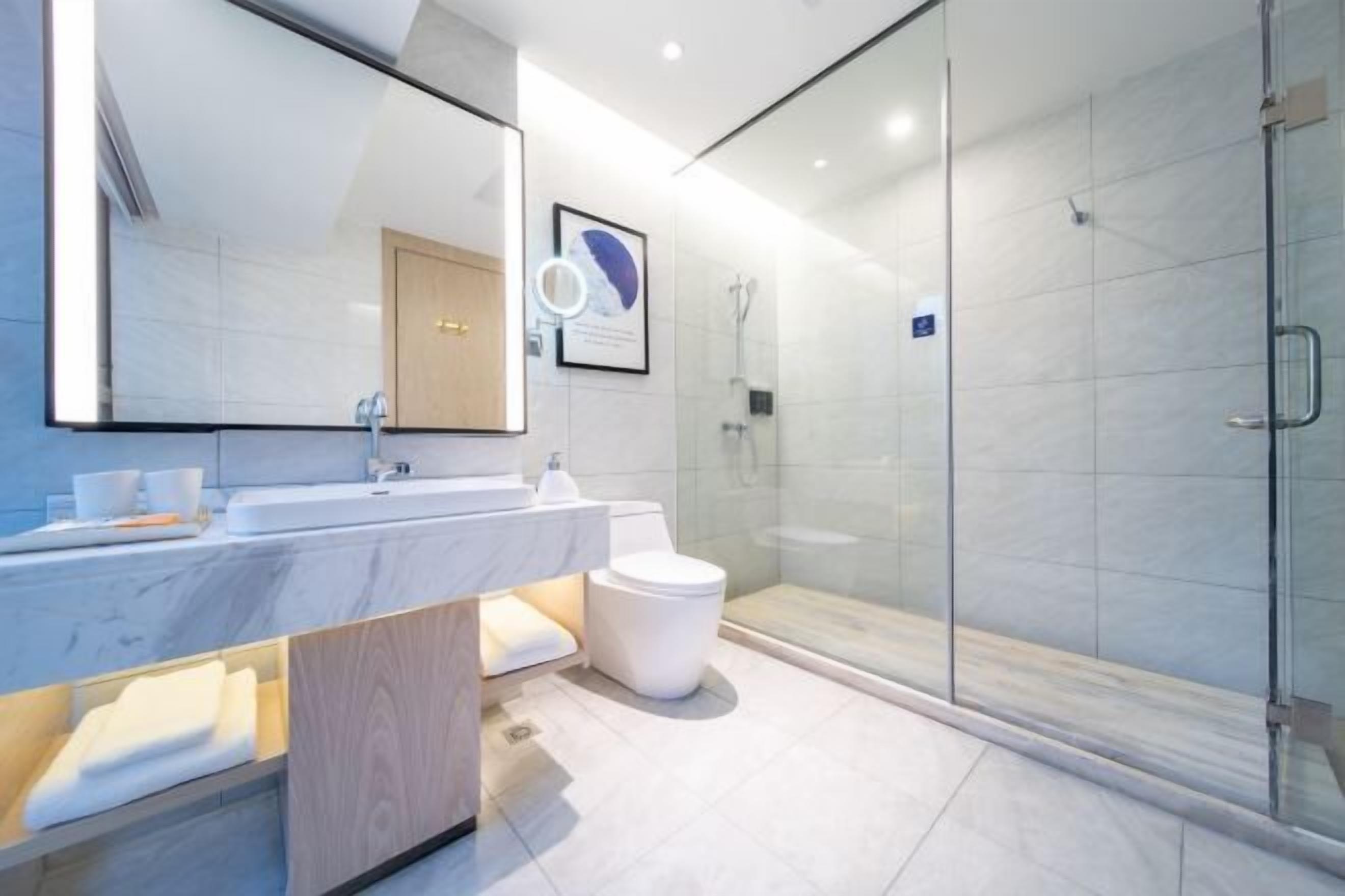 A modern bathroom with a glass shower enclosure, a marble sink, and a large mirror.