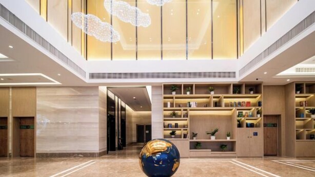 A spacious lobby with a central globe sculpture, high ceilings, and modern shelving with plants. - Kyriad Hotel (Zijin Wanhui Branch) (Zijin)