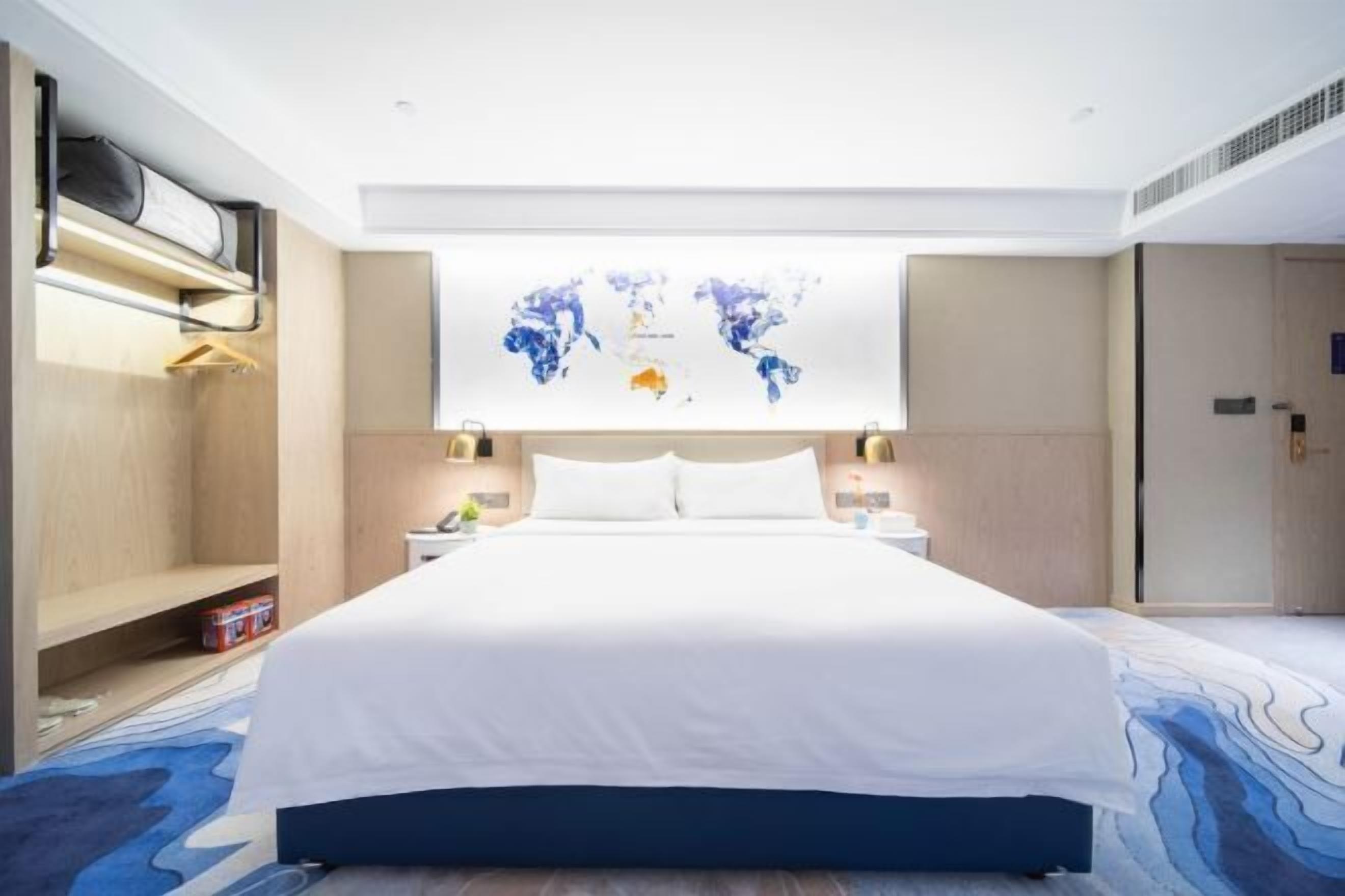 A hotel room with a bed, a world map artwork, bedside tables, and a wardrobe.
