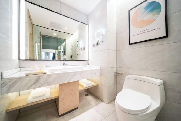 Une salle de bain moderne avec un grand miroir, un lavabo, des toilettes et une œuvre d’art encadrée accrochée au mur.