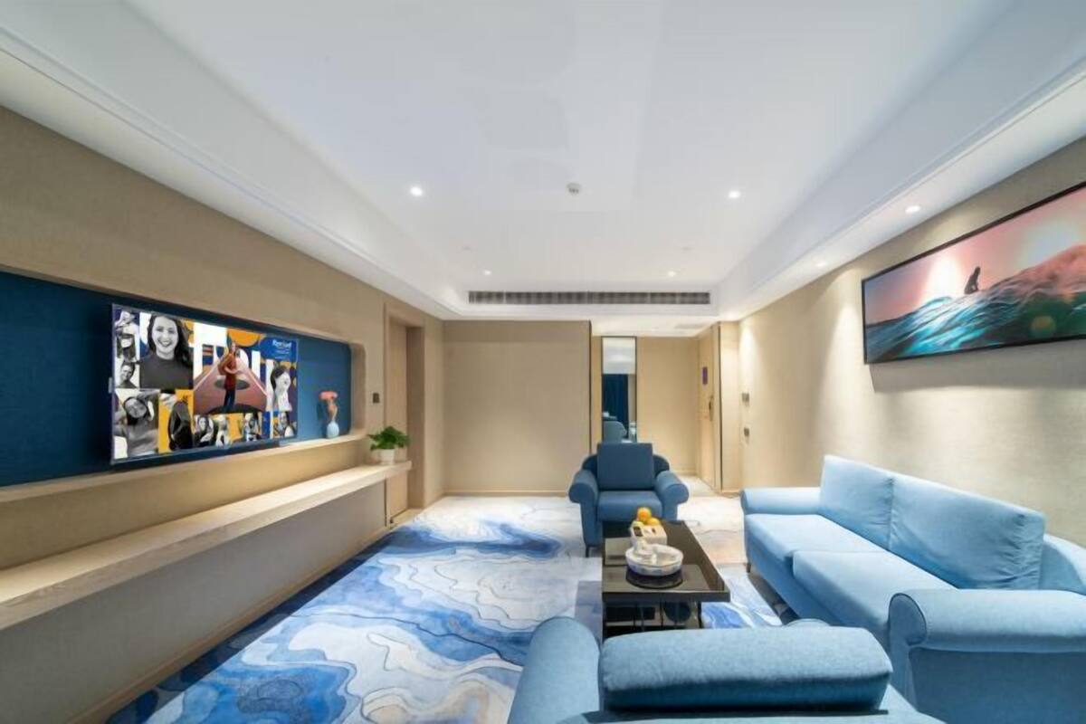 A modern hotel room with a blue sofa, a coffee table, and a wall-mounted TV.