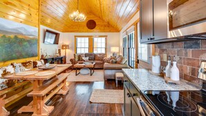 L’intérieur chaleureux d’un chalet avec un plafond en bois, un coin repas avec des bancs, un salon doté d’un canapé et une cuisine équipée d’une cuisinière.