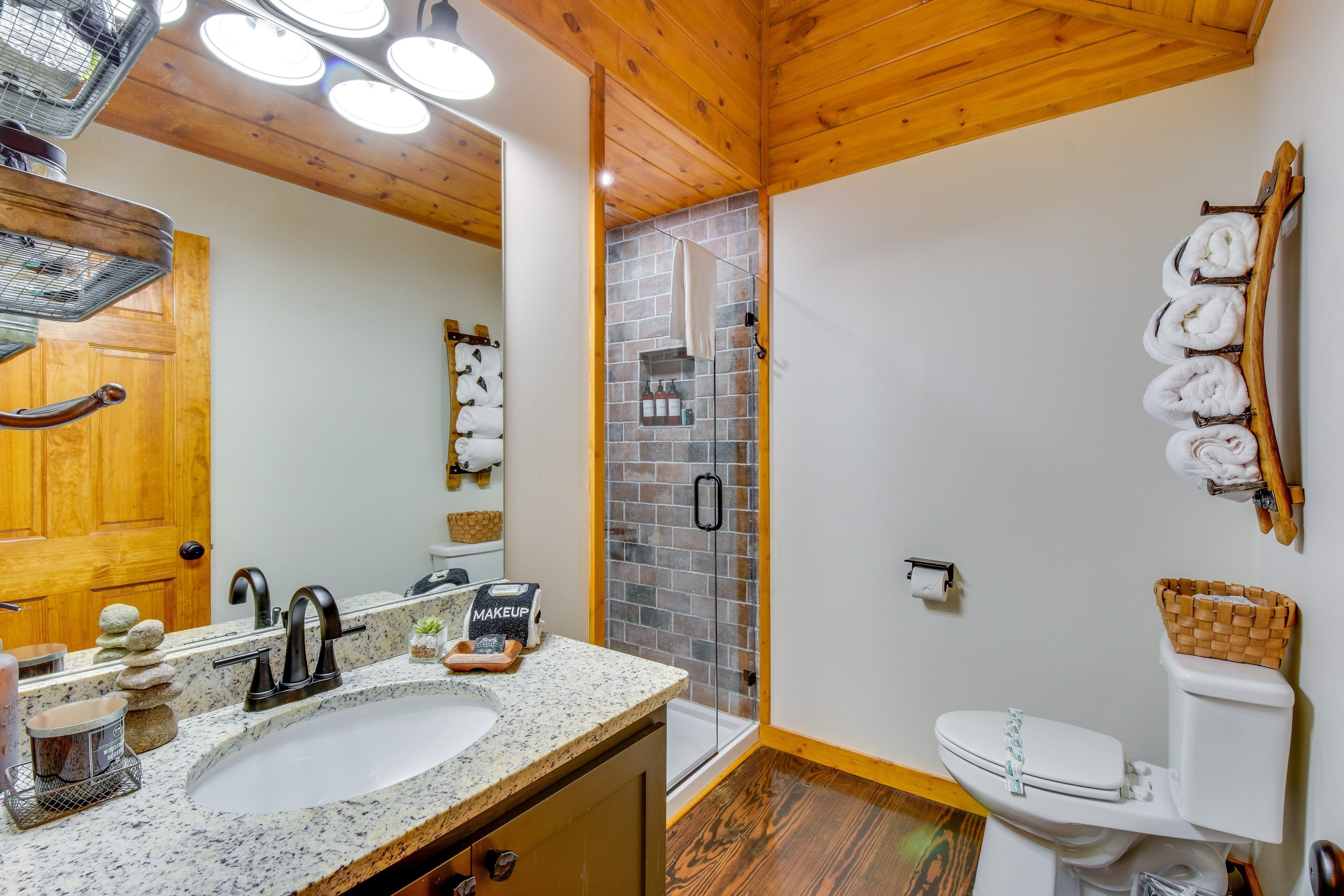 Un baño con techo de madera, un lavamanos con espejo, una ducha con puerta de vidrio y un inodoro con toallas en la pared.