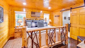 Une chambre dans une cabane en bois, avec un lit, des tables de chevet et une grande fenêtre.
