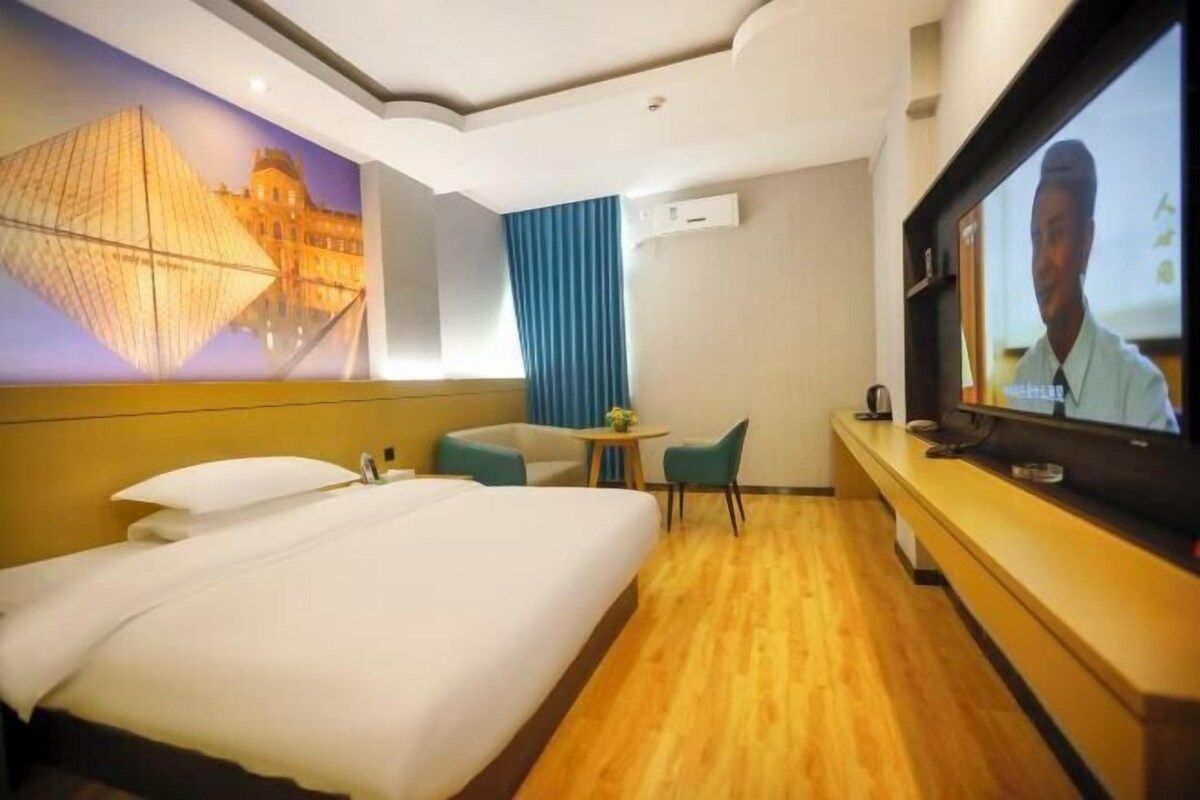 A hotel room with a large bed, a desk with a television, a small table with chairs, and a mural of a building.