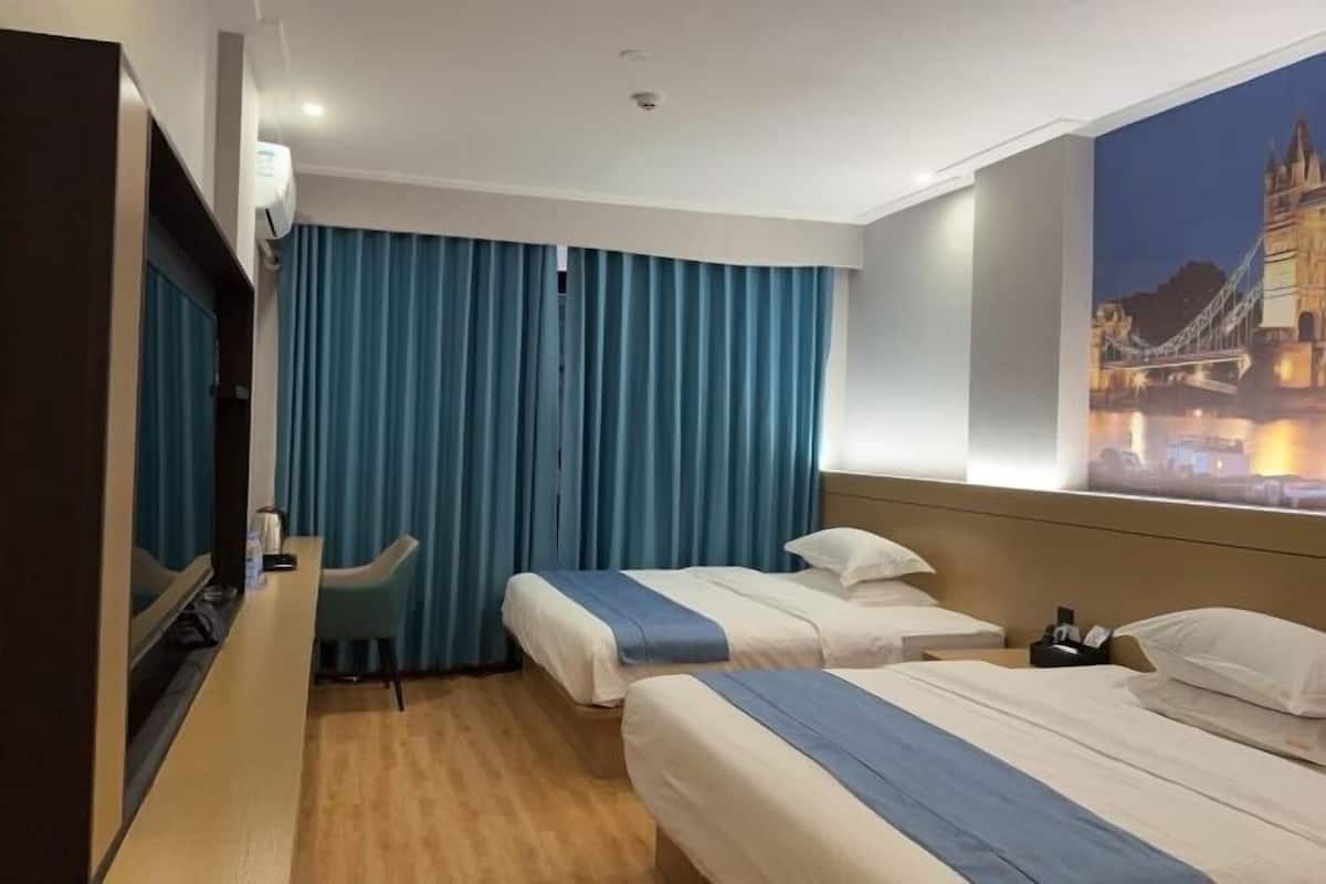 Habitación de hotel con dos camas, un escritorio, una silla y un ventanal con vista a un puente.