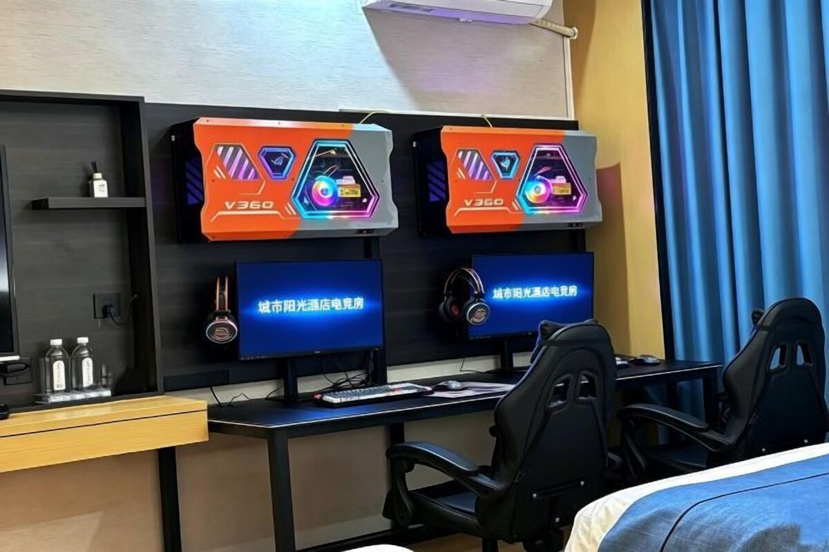 A hotel room with two monitors, a desk, and a chair.