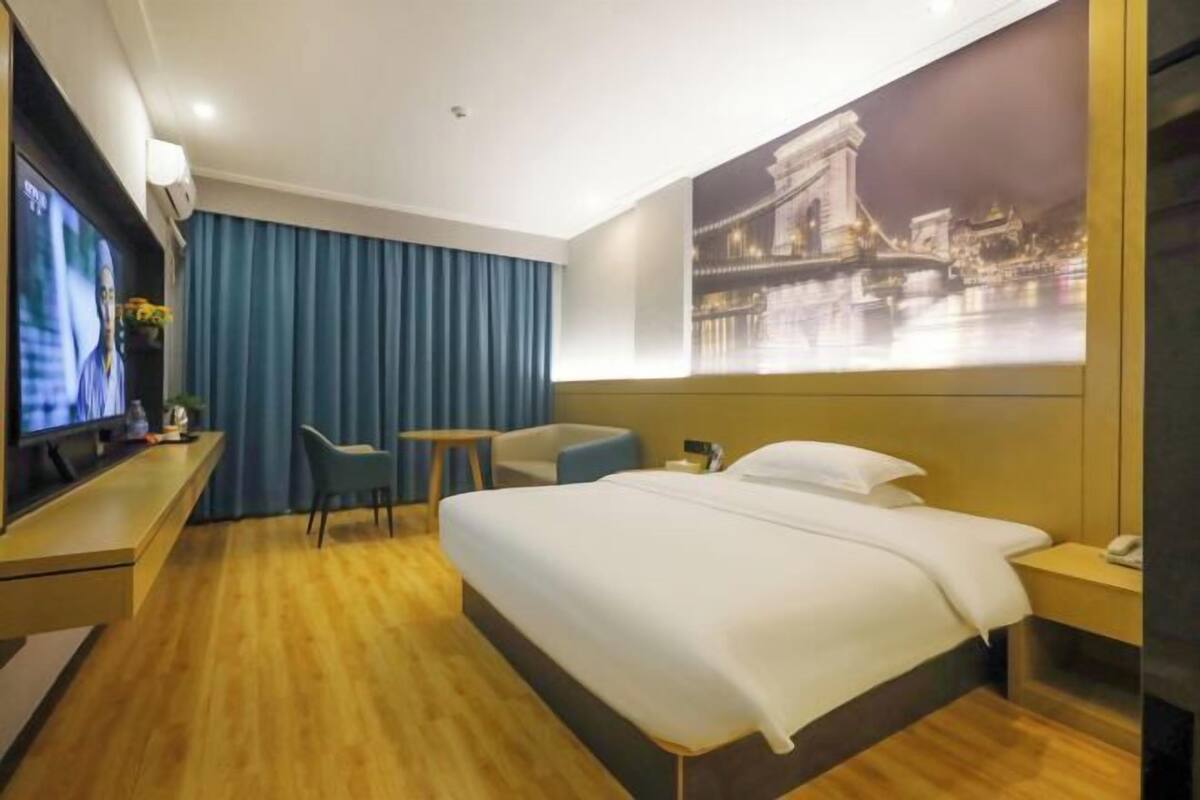 Habitación de hotel con cama, escritorio, silla, televisor y una obra de arte colgada en la pared.