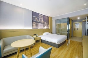 Una habitación de hotel con cama, sofá, una mesita y una partición de vidrio.