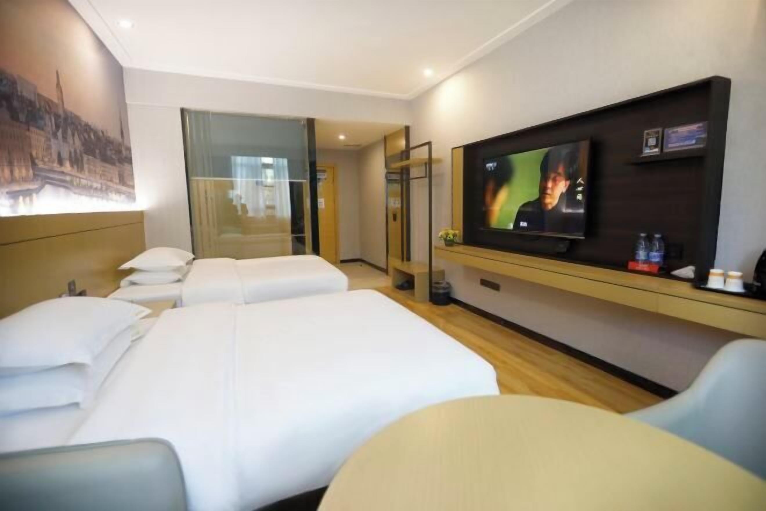 Habitación de hotel con dos camas, televisión, escritorio y separador de vidrio.