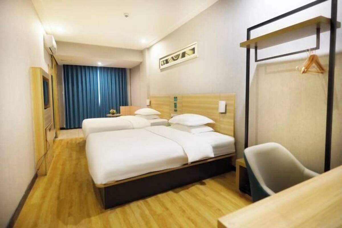 Una habitación de hotel con una cama, una silla, un escritorio, un armario y una cortina.