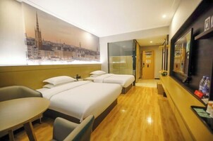 A hotel room with a large bed, a desk, a chair, a TV, and a cityscape mural on the wall.