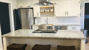 Una cocina moderna con armarios blancos, un refrigerador de acero inoxidable, un horno empotrado e isla central con taburetes de bar.