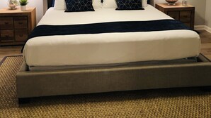 Un dormitorio con cabecera capitonada, una cama grande con ropa de cama blanca y azul oscuro, dos mesitas de noche con lámparas y un ventilador de techo.