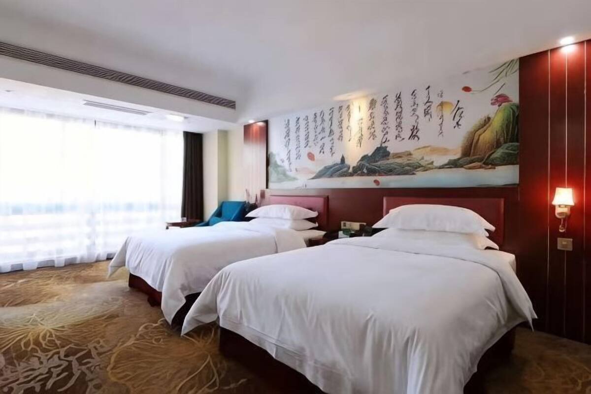 A hotel room with two beds, a large painting on the wall, and a view of the outdoors.