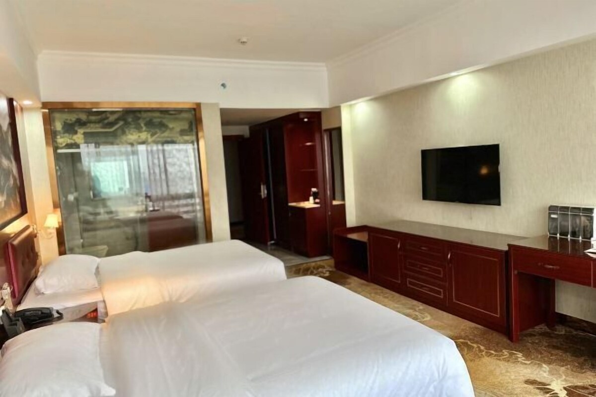 Una habitación de hotel con dos camas, un televisor, un escritorio y un espejo grande.