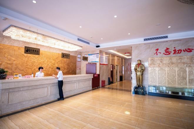 A hotel reception area with a receptionist, a reception desk, and a statue.