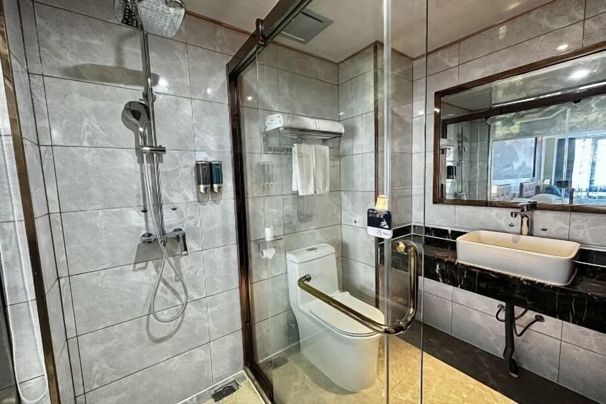 Un baño moderno con ducha envuelta en cristal, un inodoro blanco, un lavamanos y un espejo grande.