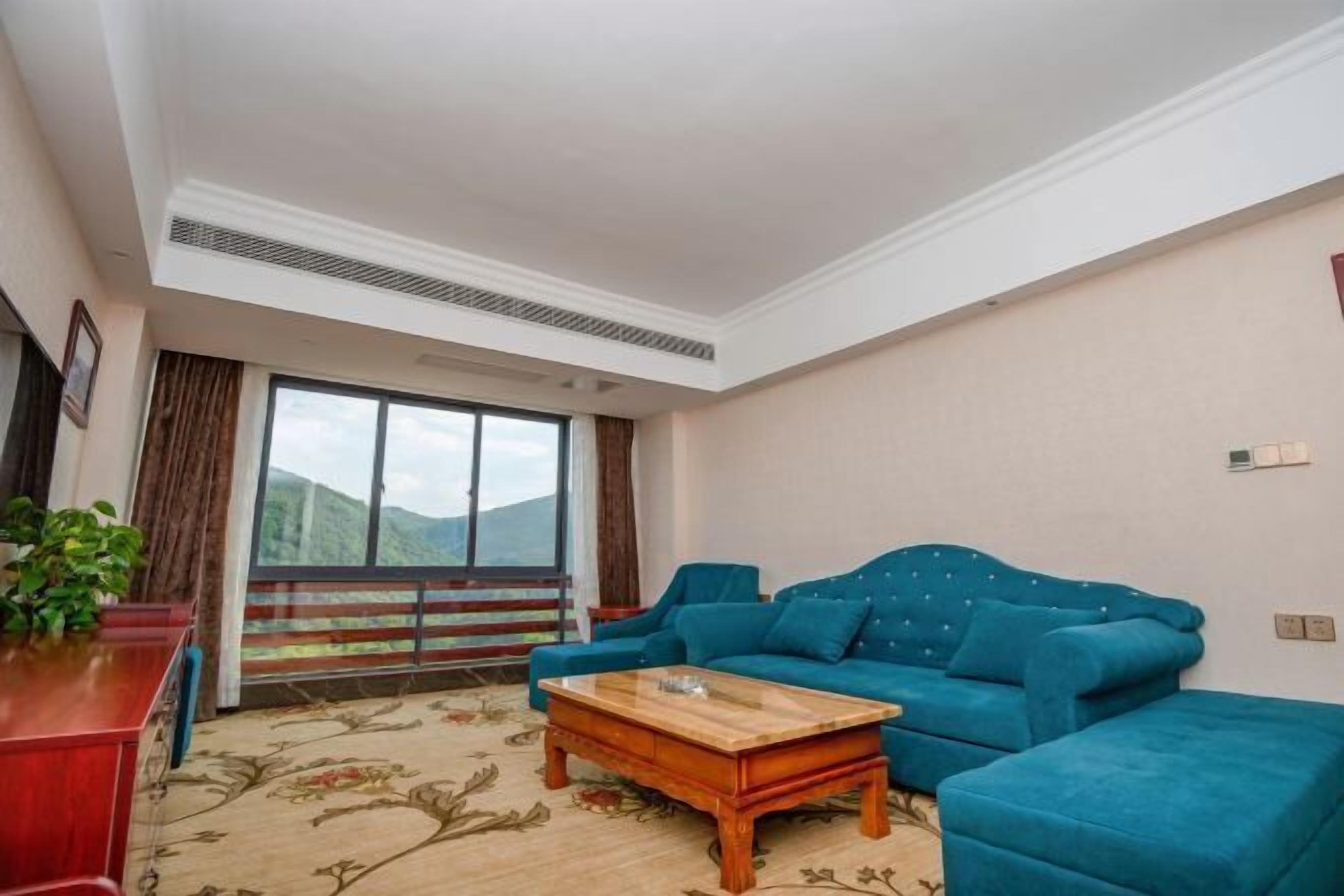 A living room with a sofa, a coffee table, a red cabinet, and a large window with a view of mountains.