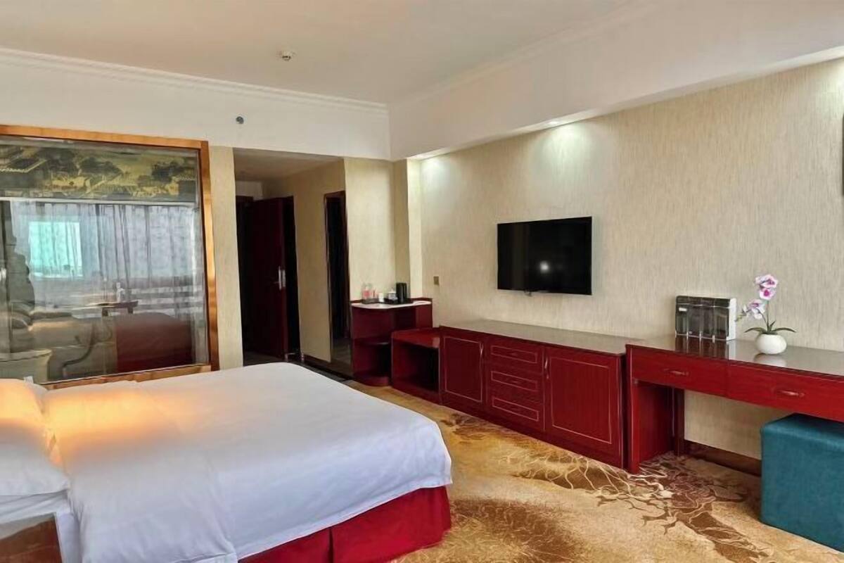 A hotel room with a bed, a desk, a TV, and a large window.