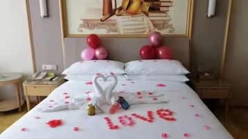 A hotel room with a bed adorned with rose petals and a heart-shaped arrangement of towels.