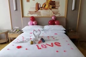 Ein Hotelzimmer mit einem Bett, dekoriert mit Rosenblättern und einer herzförmigen Handtuchanordnung.