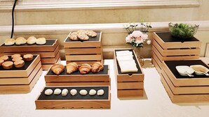 A display of various baked goods in wooden crates, arranged on a table in a room with a decorative wall and a vase of flowers. - Vienna Hotel (Jiujiang Duchangxin Bus Station) (Duchang)