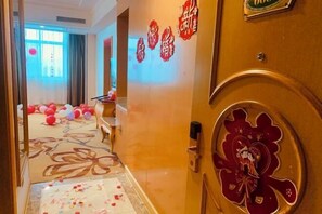 Ein Hotelkorridor mit einem floralen Teppich, einer Holztür mit dekorativem Wappen und roten Wandgestaltungen.