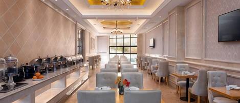 A hotel dining area with a buffet, seating, and a chandelier.