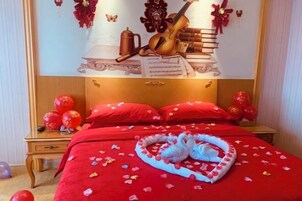 Habitación de hotel con una colcha roja, una toalla con forma de cisne y almohadas rojas.