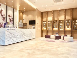 A modern reception area with a marble counter, a flat-screen TV, and a display of products on shelves. - Lavande Hotel (Foshan)