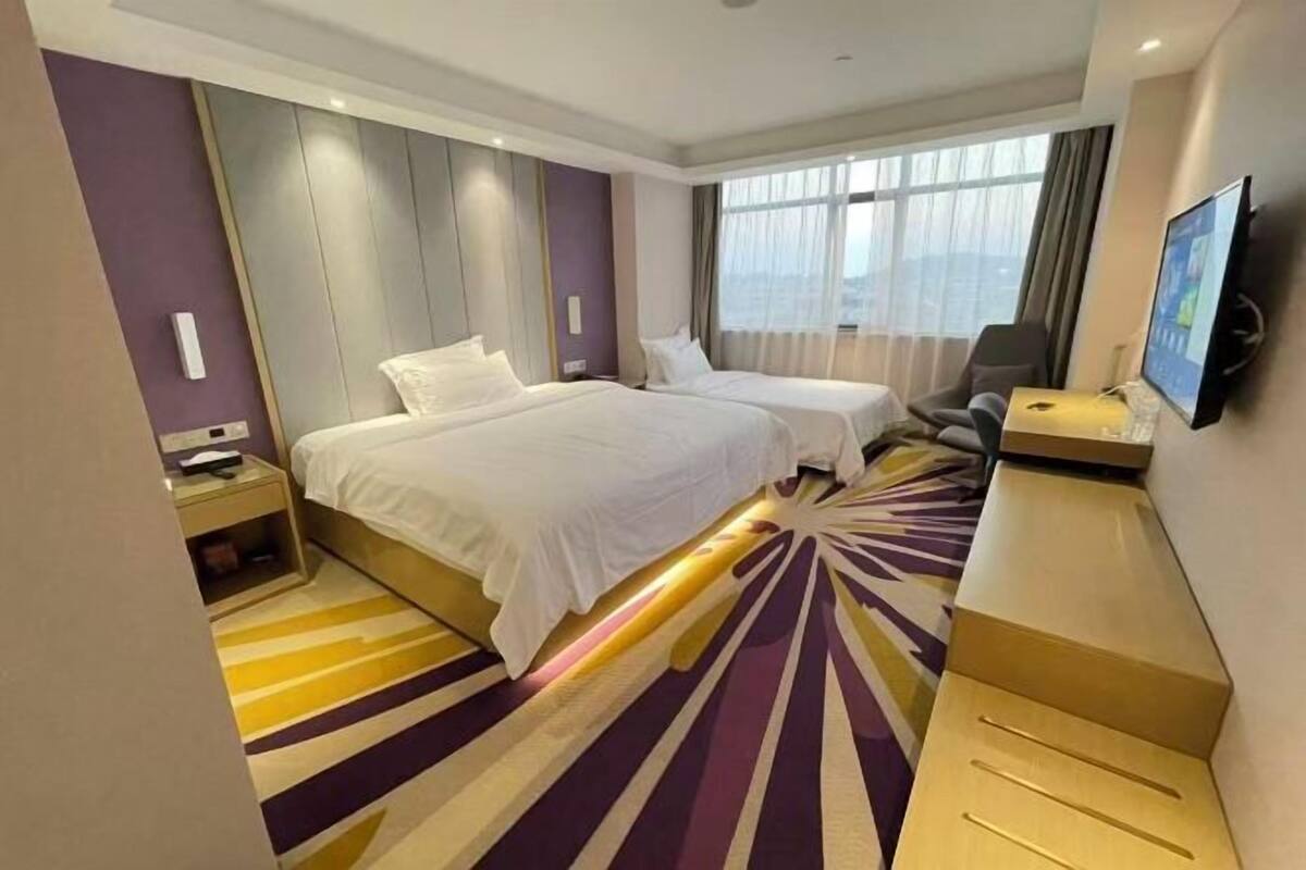 A hotel room with two beds, a desk with a computer, a TV, and a large window.