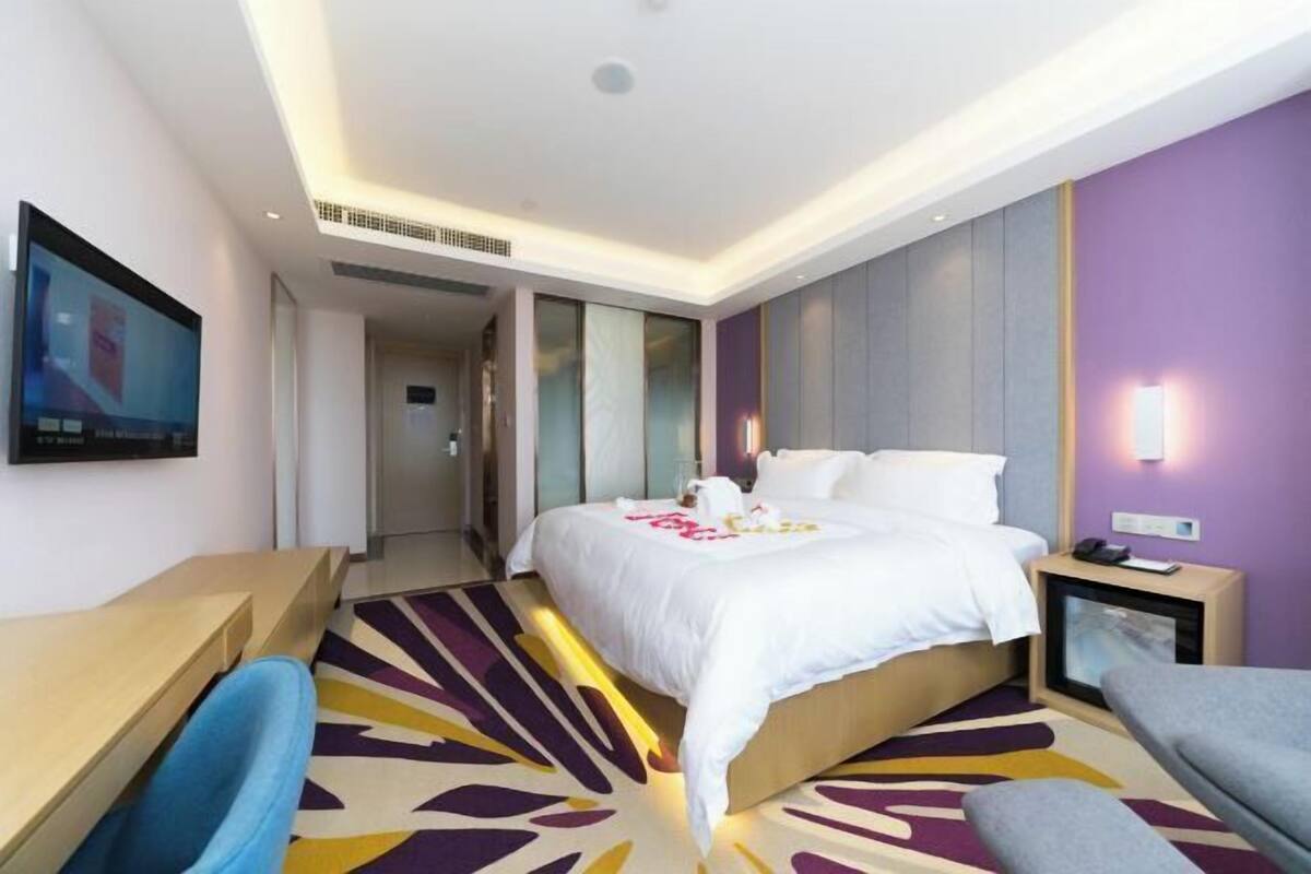 A hotel room with a bed, a desk, a chair, a TV, and a bedside table.