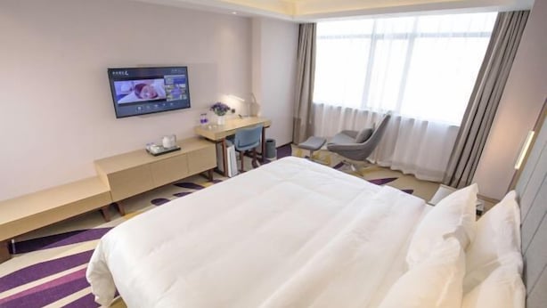 A hotel room with a large bed, a desk with a computer, a chair, and a TV mounted on the wall. - Lavande Hotel (Foshan)