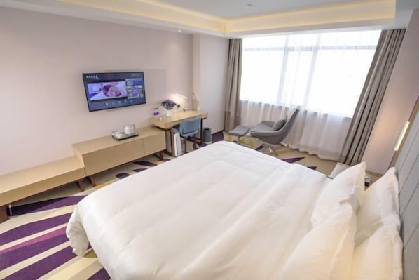 A hotel room with a large bed, a desk with a computer, a chair, and a TV mounted on the wall. - Lavande Hotel (Foshan)