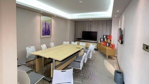 A conference room with a long table, white chairs, a flat-screen TV, and a small display unit with various items. - Lavande Hotel (Foshan South Railway Station Bijiang Light Rail Station) (Foshan)
