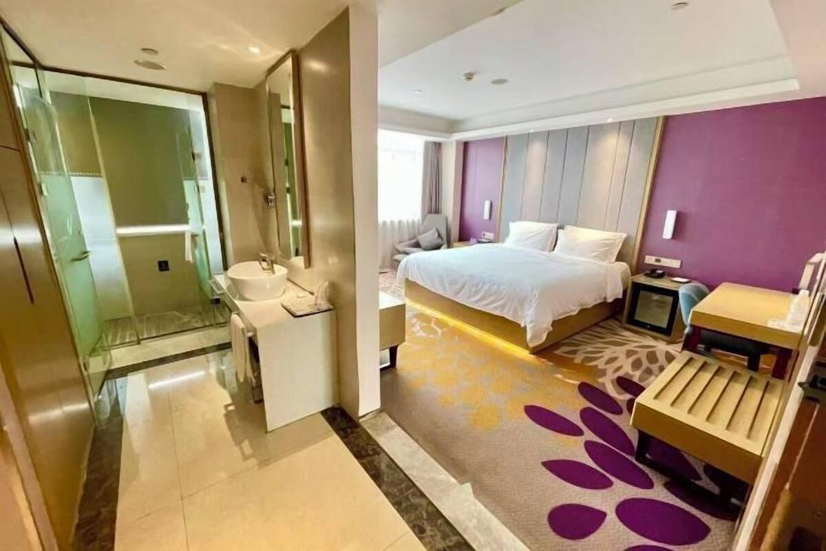 A hotel room with a bed, bedside table, TV, and a bathroom with a shower and sink.