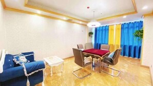 A room with a blue sofa, a dining table with four chairs, a small white table, and a ceiling light. - Lavande Hotel (Foshan)
