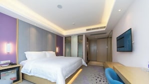 A modern hotel room with a bed, bedside table, desk, and a TV mounted on the wall. - Lavande Hotel (Foshan)